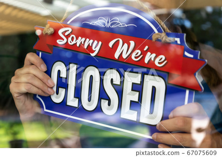 Female Store Owner Turning Sign to Closed in Storefront Window 67075609