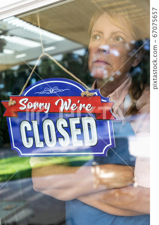 Female Store Owner Turning Sign to Closed in Storefront Window Female Store Owner Turning Sign to Closed in Storefront Window 67075657