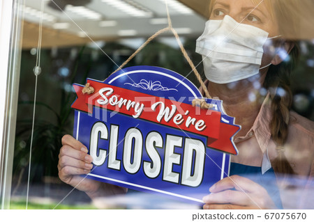 Female Store Owner Turning Sign to Closed in Storefront Window 67075670