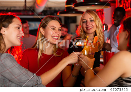 Chatting friends holding cocktails and laughing in nightclub 67075823