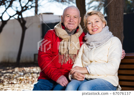 Mature couple sitting in park Mature couple sitting in park 67076137