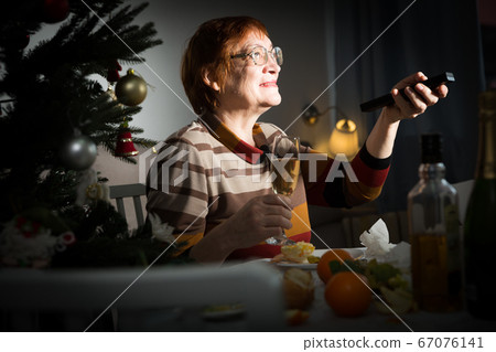Smiling mature woman watching Christmas tv program Smiling mature woman watching Christmas tv program 67076141