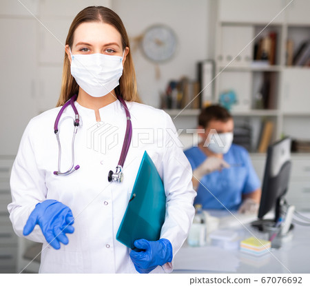 Portrait of female doctor in lab coat and protective medical masks holding clipboard Portrait of female doctor in lab coat and protective medical masks holding clipboard 67076692