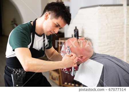 Portrait of young man barber shaving man's head Portrait of young man barber shaving man's head 67077314