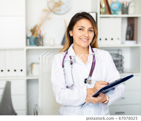 Female doctor in medical coat holding clipboard in clinic Female doctor in medical coat holding clipboard in clinic 67078025