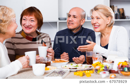 Smiling aged friends are sitting at table with tea and talking about life Smiling aged friends are sitting at table with tea and talking about life 67078929