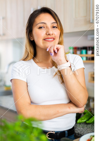 Woman is standing near table and cutting vegetables in the kitchen at the home Woman is standing near table and cutting vegetables in the kitchen at the home 67079160