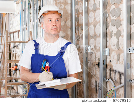Focused construction worker inspecting room and planning upcoming repairs Focused construction worker inspecting room and planning upcoming repairs 67079513