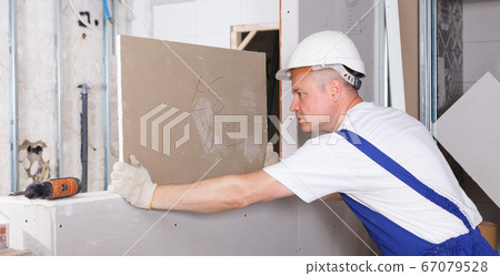 Worker engaged in drywall mounting Worker engaged in drywall mounting 67079528
