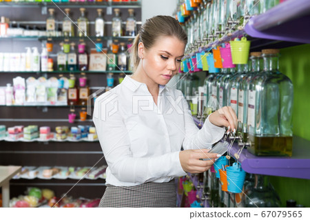 Young salesgirl offering perfume on tap in modern perfumery 67079565
