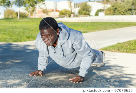 Athletic young male in sportswear training different exercises at park 67079633