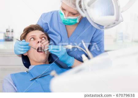 Male patient sitting on chair in dental office getting dentist treatment Male patient sitting on chair in dental office getting dentist treatment 67079638