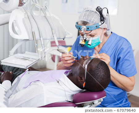Dentist professional filling teeth for man patient sitting in medical chair Dentist professional filling teeth for man patient sitting in medical chair 67079640