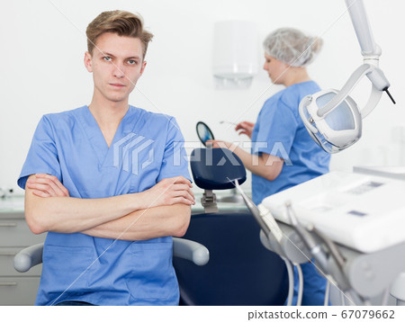 Portrait of professional male dentist with arms crossed with dental assistant background Portrait of professional male dentist with arms crossed with dental assistant background 67079662