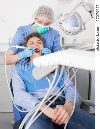 Male patient sitting on chair in dental office getting dentist treatment 67079675