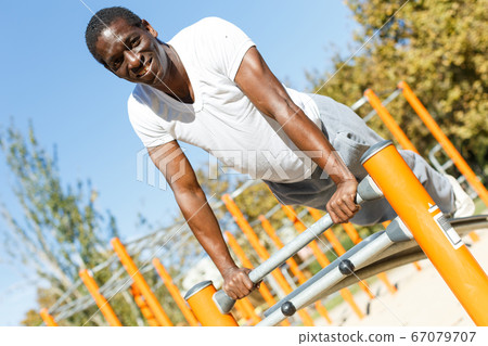 Active african american man doing workout at pull-up bar in park 67079707