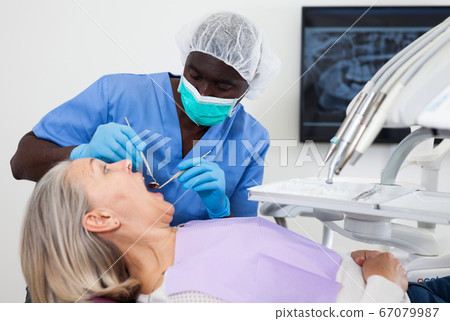 Dentist is treating female patient which is sitting in dental chair in clinic Dentist is treating female patient which is sitting in dental chair in clinic 67079987