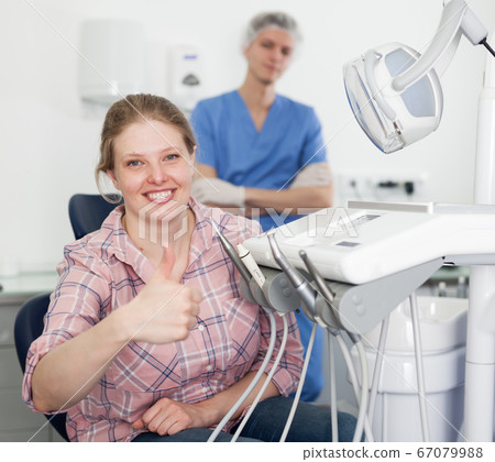 Portrait of smiling satisfied woman visiting dentist giving thumbs up in the dental clinic Portrait of smiling satisfied woman visiting dentist giving thumbs up in the dental clinic 67079988