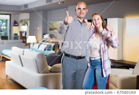 Portrait of man and woman with thumbs up in furniture salon Portrait of man and woman with thumbs up in furniture salon 67080169