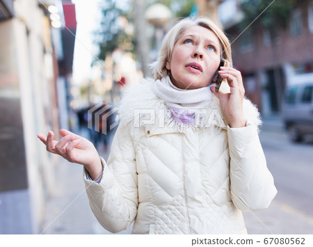 Mature woman is talking by phone in time walking Mature woman is talking by phone in time walking 67080562