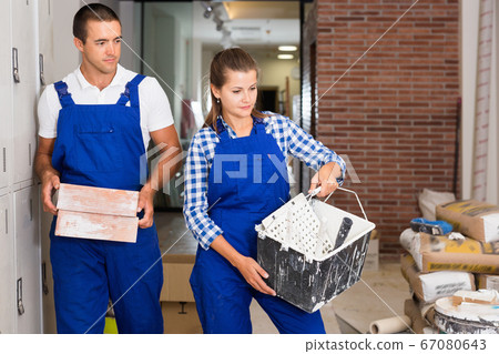 Man and woman in work overalls doing finishing work in room of public space Man and woman in work overalls doing finishing work in room of public space 67080643