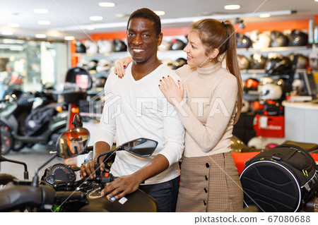 Happy young couple satisfied with choice in modern motorcycle salon Happy young couple satisfied with choice in modern motorcycle salon 67080688