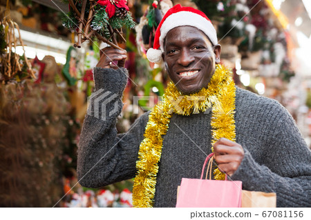 Guy in Santa hat choosing Christmas decorations Guy in Santa hat choosing Christmas decorations 67081156