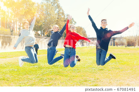 Four joyful teens jump on a lawn 67081491