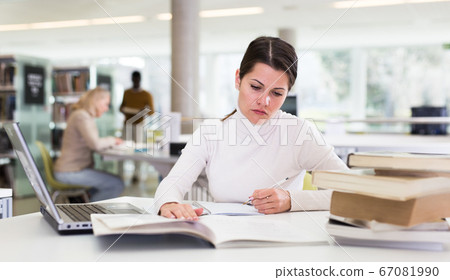 Adult female student with laptop and books in public library 67081990