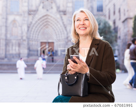 Business woman dialing message on mobile phone sitting on a street bench 67081991