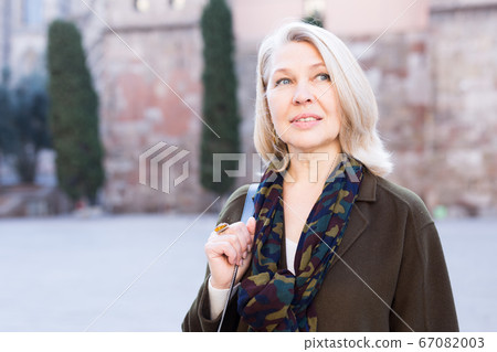 Elegant mature woman is posing in time walking on the street of old city 67082003