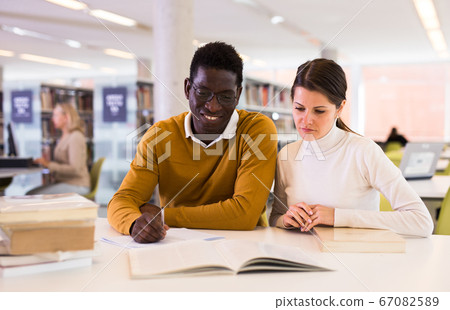 Portrait of couple of adult students studying together in public library 67082589