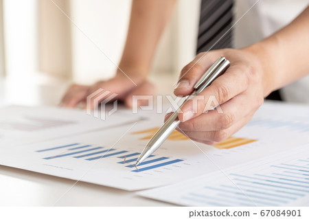 A businessman is sitting at a desk and calculating financial graphs about real estate investment expenditures A businessman is sitting at a desk and calculating financial graphs about real estate investment expenditures 67084901