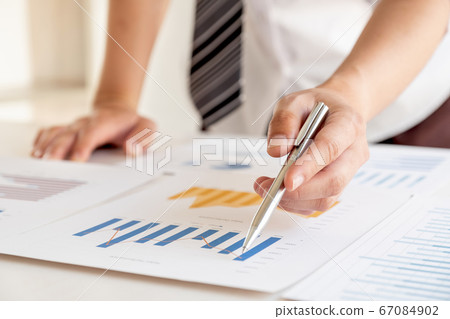 A businessman is sitting at a desk and calculating financial graphs about real estate investment expenditures A businessman is sitting at a desk and calculating financial graphs about real estate investment expenditures 67084902