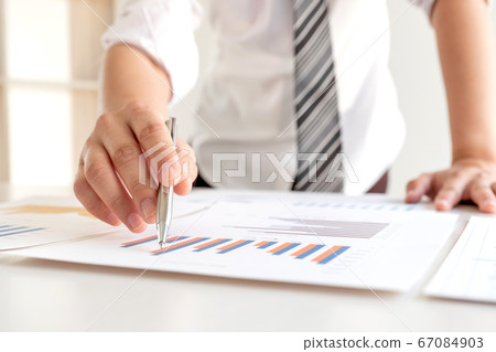A businessman is sitting at a desk and calculating financial graphs about real estate investment expenditures A businessman is sitting at a desk and calculating financial graphs about real estate investment expenditures 67084903