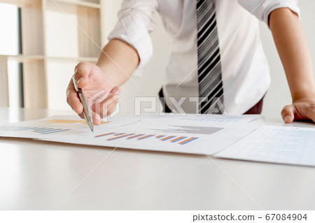 A businessman is sitting at a desk and calculating financial graphs about real estate investment expenditures A businessman is sitting at a desk and calculating financial graphs about real estate investment expenditures 67084904