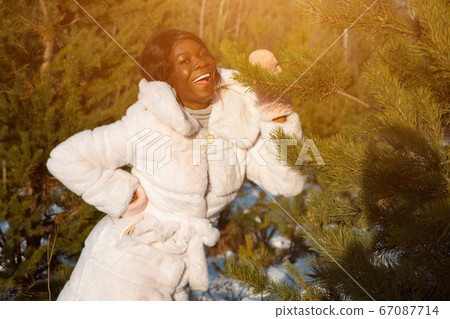 Dark-skinned woman in a white fur coat in a winter forest sunlight 67087714