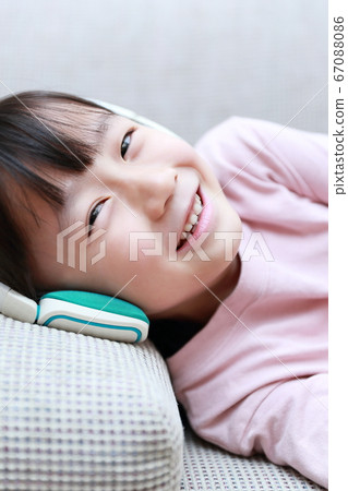 Girl lying on the sofa while listening to music on headphones Girl lying on the sofa while listening to music on headphones 67088086