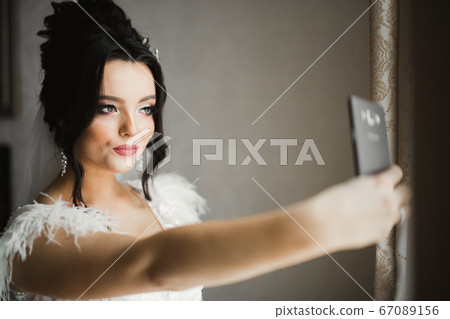 A sweet smiling bride in a light interior makes selfie on the phone A sweet smiling bride in a light interior makes selfie on the phone 67089156