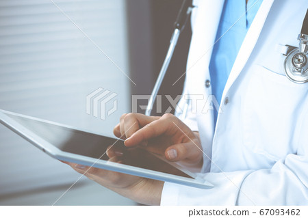 Woman doctor using white tablet computer while sitting at chair in hospital, close-up 67093462