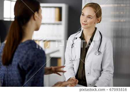 Cheerful smiling female doctor and patient woman discussing current health examination while sitting in clinic. Perfect medical service in hospital. Medicine concept 67093816
