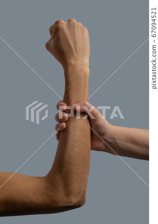 Close-up of light-skinned hand clenching dark-skinned forearm Close-up of light-skinned hand clenching dark-skinned forearm 67094521