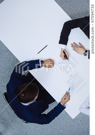 Group of business people and lawyer discussing contract papers sitting at the table, view from above. Businessman is signing document after agreement done Group of business people and lawyer discussing contract papers sitting at the table, view from above. Businessman is signing document after agreement done 67094738