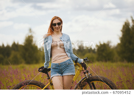 Attractive young woman in sportswear in a flower field with bike Attractive young woman in sportswear in a flower field with bike 67095452