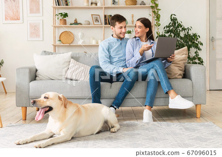 Young happy couple sitting on sofa with their dog 67096015