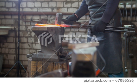 Muscular man blacksmith with hammer in forge creating steel knife Muscular man blacksmith with hammer in forge creating steel knife 67096556