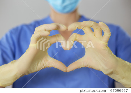 Hands in rubber gloves making the heart symbol in front of a healthcare professional in uniform. Hands in rubber gloves making the heart symbol in front of a healthcare professional in uniform. 67096937