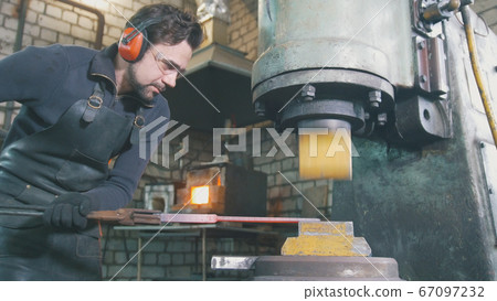 Molten metal is processed under pressure in the hands of a blacksmith 67097232