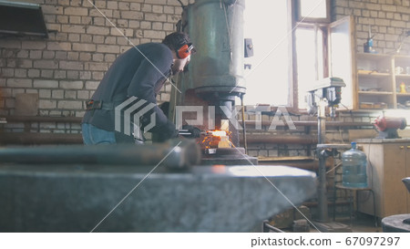 Molten metal is processed under pressure in the hands of a blacksmith, wide angle Molten metal is processed under pressure in the hands of a blacksmith, wide angle 67097297