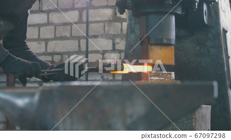 Man blacksmith forges the metal at the mechanical hammer Man blacksmith forges the metal at the mechanical hammer 67097298